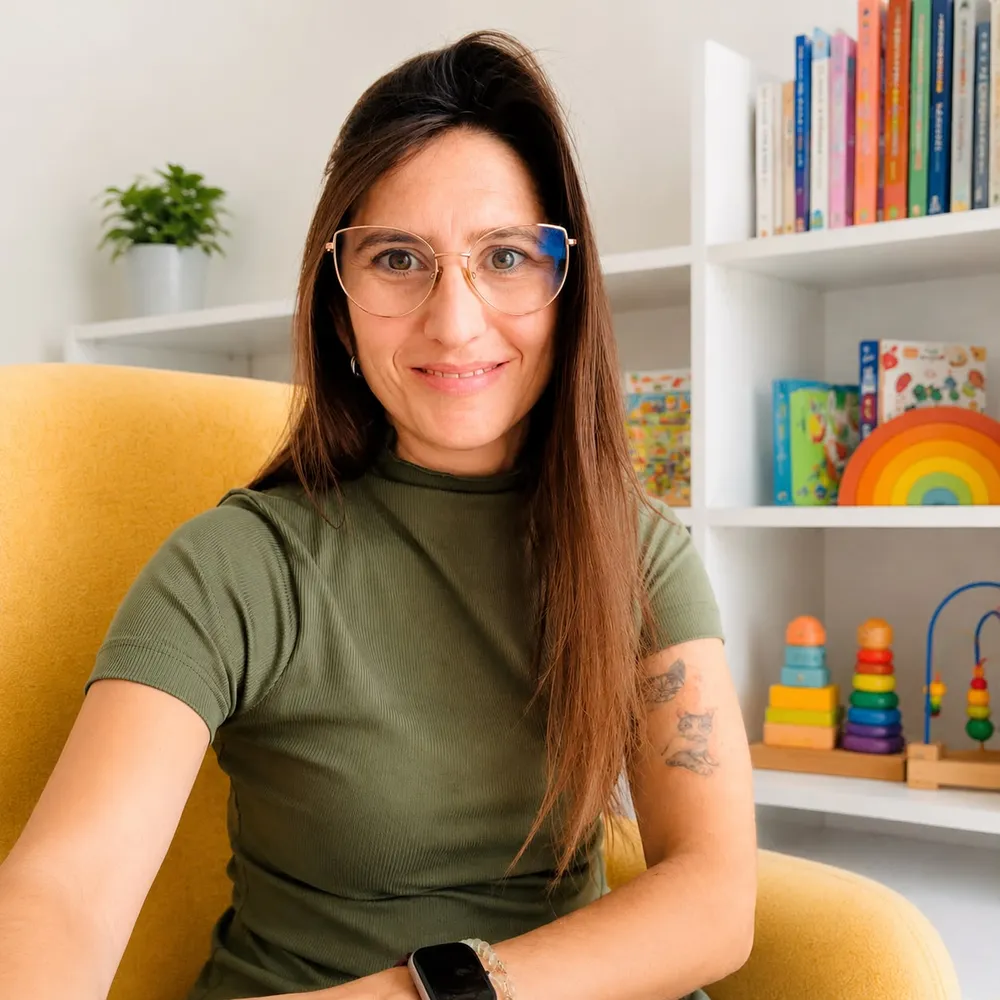 Ani, de l'equip d'Espai Tribu, somrient asseguda en una butaca groga davant una prestatgeria de jocs i llibres infantils.