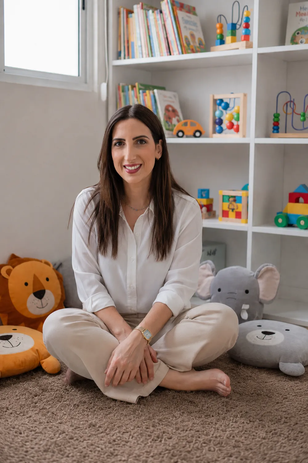 Sandra, fundadora d'Espai Tribu, asseguda a terra amb les cames creuades, entre peluixos d'animals, a la sala de joc.