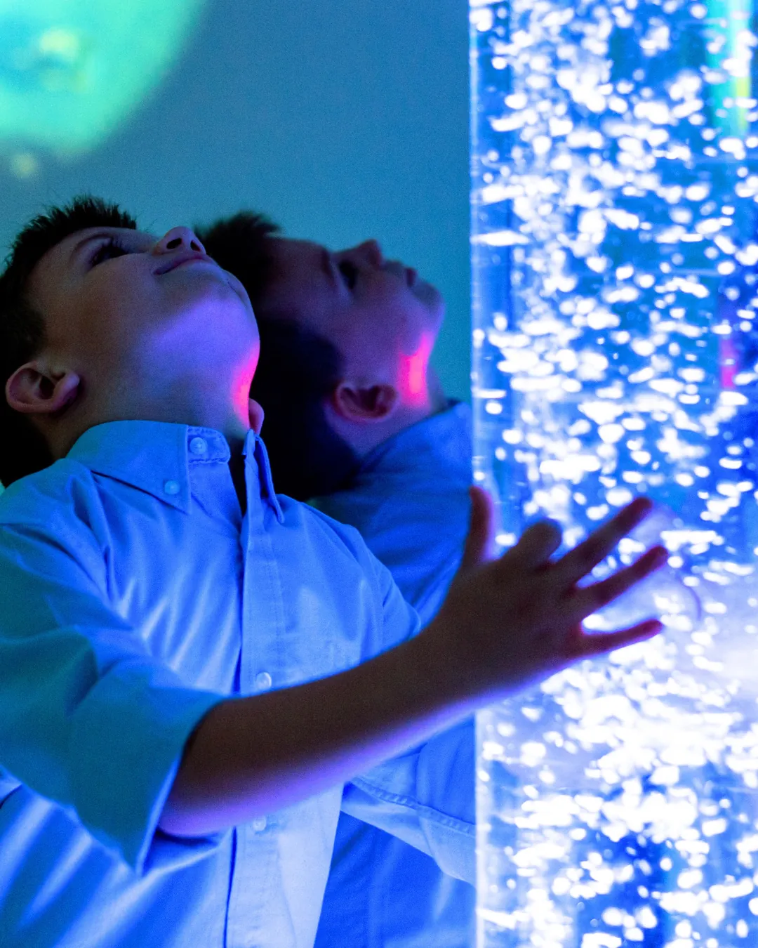 Un infant explora una columna de bombolles il·luminada en una sala d'estimulació sensorial.