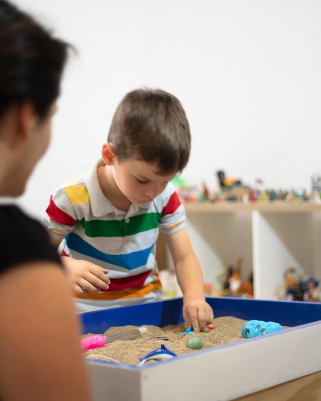 Un infant i una acompanyant juguen amb sorra cinètica en una taula de joc.