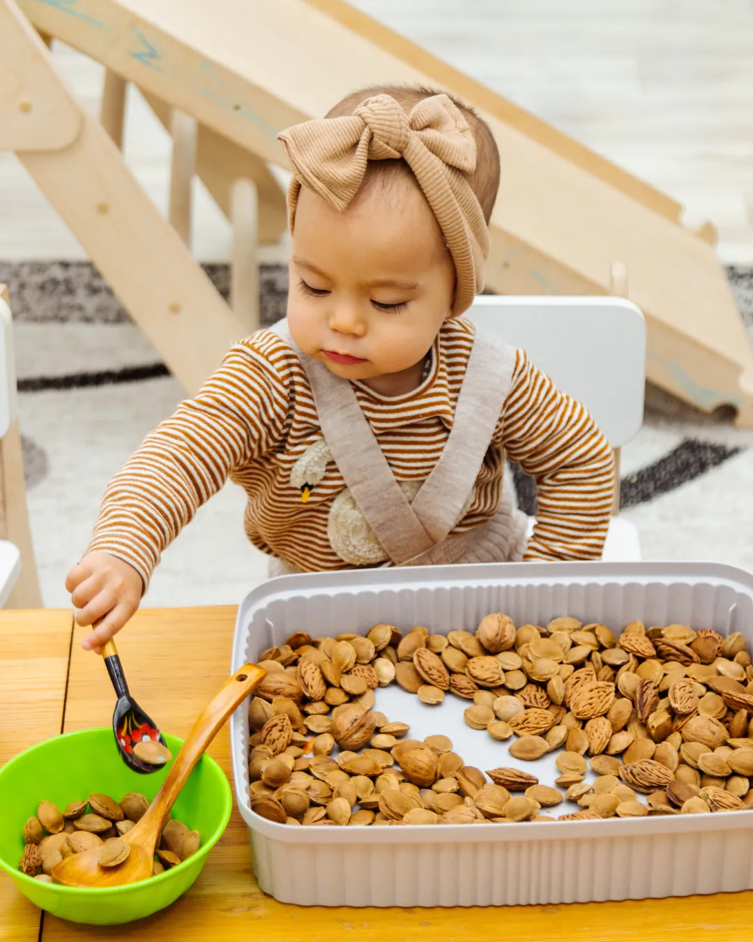 Un infant fa servir una cullera per transvasar petits fruits secs d'una safata, treballant la motricitat fina.