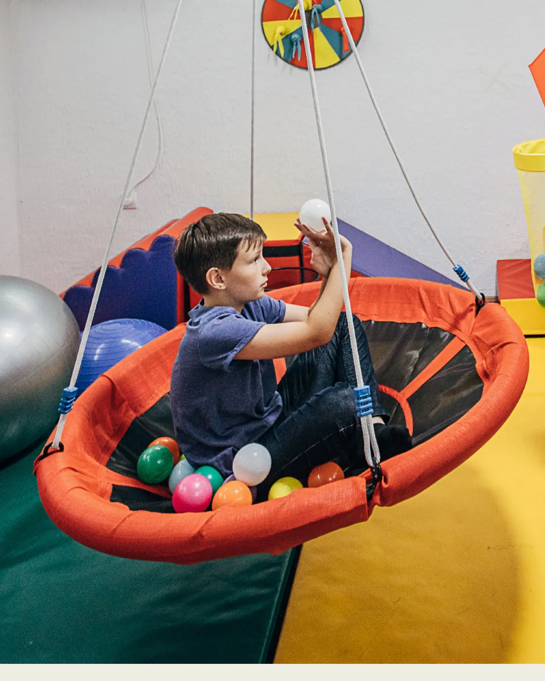 Un infant es gronxa en un gronxador de niu a la sala de psicomotricitat infantil d'Espai Tribu, a Vilanova i la Geltrú.