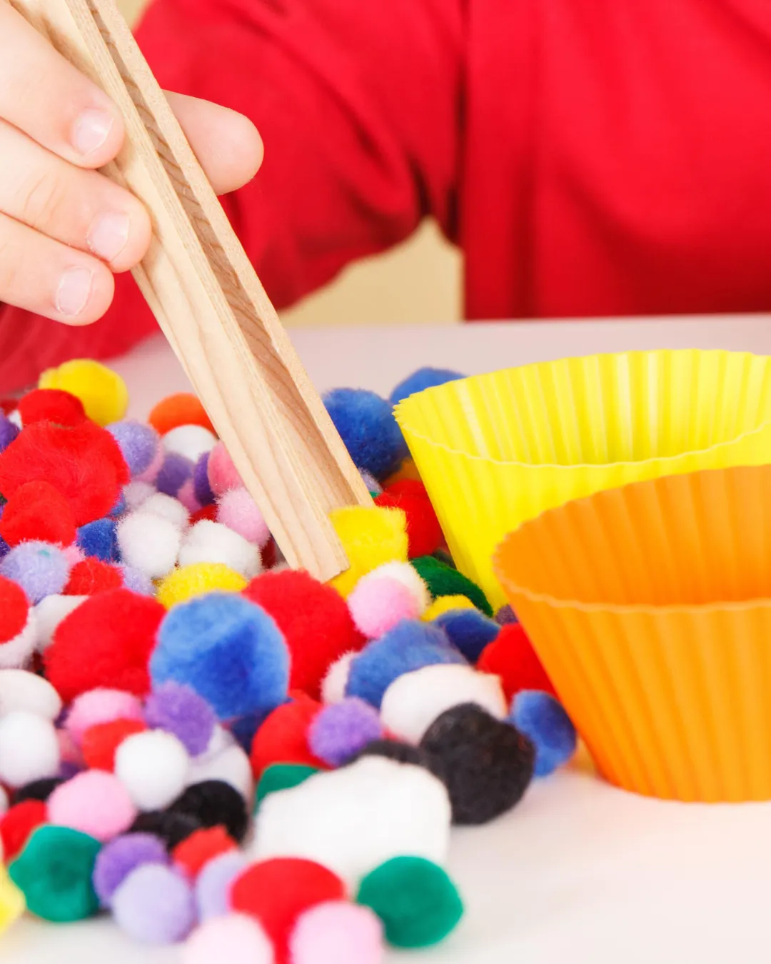 Un infant fa servir unes pinces de fusta per agafar pompons de colors, treballant la motricitat fina.